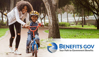 An African American woman helps a child ride a bicycle alongside Benefits.gov’s tagline: Your Path to Government Benefits.