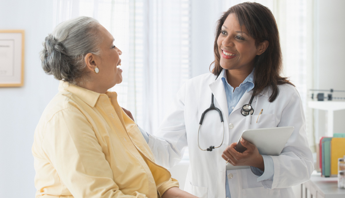 An older woman smiles as she speaks to her female African American doctor.