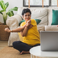 Woman stretches arms while seated on the floor in front of a sofa.