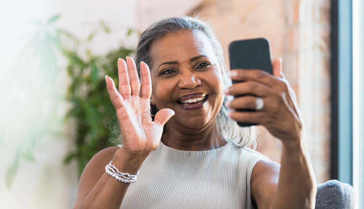 A woman smiling and waving at someone on the other end of her video call on her smartphone